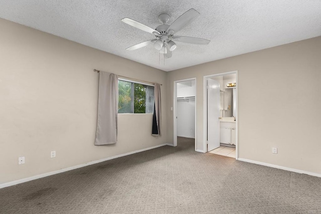 unfurnished bedroom with a walk in closet, a textured ceiling, carpet, and baseboards