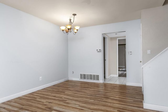 empty room with baseboards, a notable chandelier, visible vents, and wood finished floors