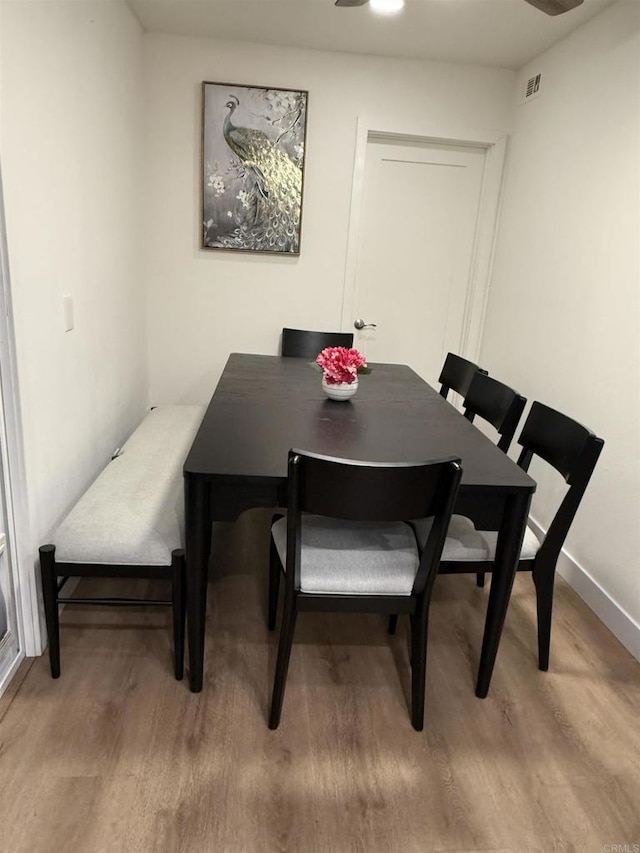 dining room featuring baseboards, a ceiling fan, visible vents, and wood finished floors