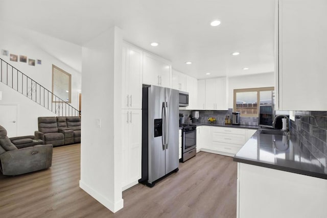 kitchen with white cabinets, appliances with stainless steel finishes, decorative backsplash, and light wood-style floors