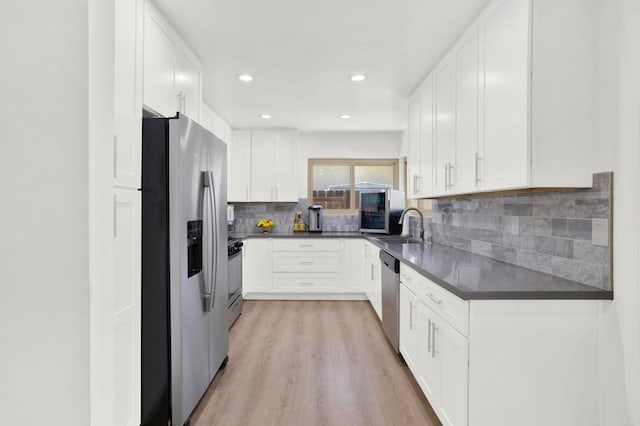 kitchen with tasteful backsplash, light wood finished floors, dark countertops, stainless steel appliances, and white cabinets