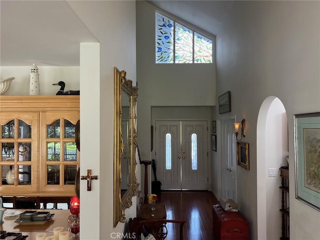 foyer with a high ceiling, arched walkways, and wood finished floors