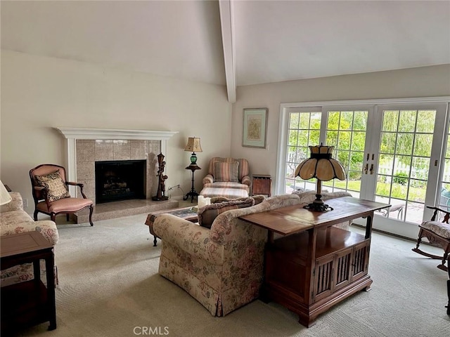 living room featuring light carpet, a wealth of natural light, a tiled fireplace, and vaulted ceiling with beams