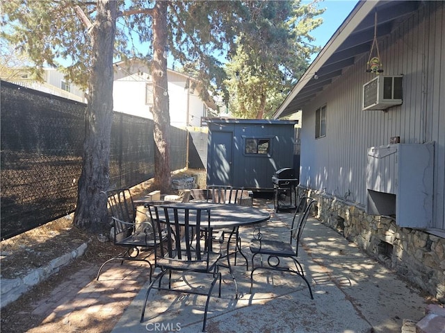 view of patio featuring an outbuilding, outdoor dining area, a wall unit AC, a shed, and a fenced backyard
