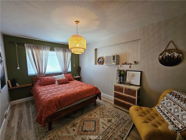 bedroom with wood finished floors, baseboards, and a wall unit AC