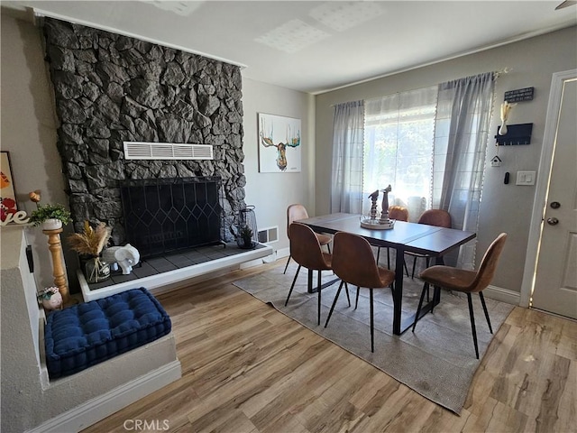 dining room featuring baseboards, a stone fireplace, visible vents, and wood finished floors