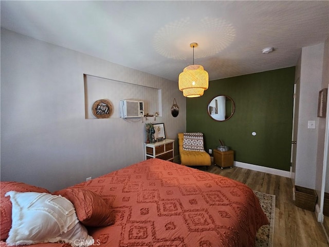 bedroom with wood finished floors, baseboards, and a wall mounted AC