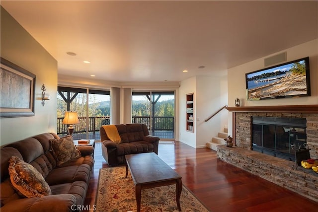 living area featuring recessed lighting, baseboards, a stone fireplace, stairs, and wood finished floors