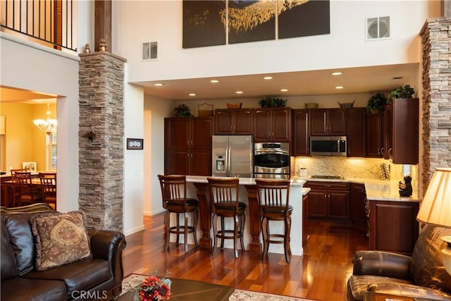 kitchen with a towering ceiling, dark wood finished floors, visible vents, and appliances with stainless steel finishes