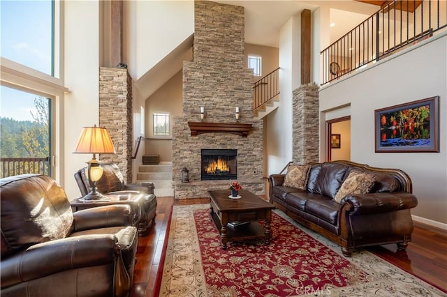 living area featuring baseboards, a towering ceiling, a stone fireplace, hardwood / wood-style flooring, and stairs
