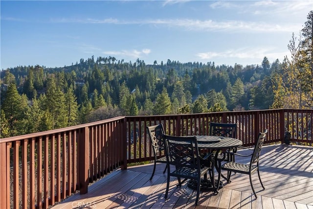 wooden deck with outdoor dining space and a forest view