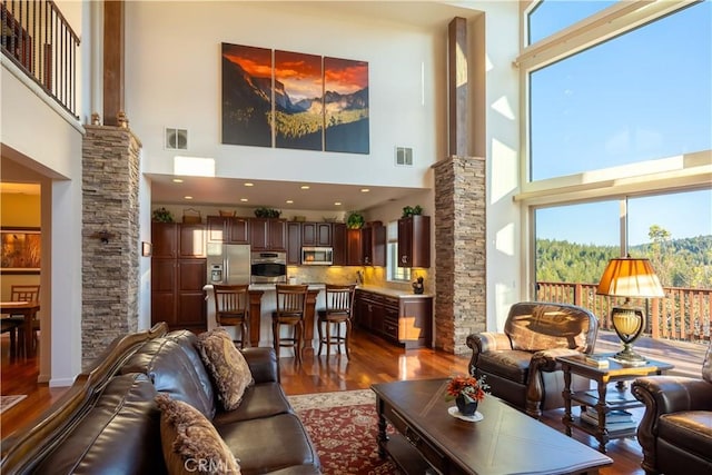 living room with ornate columns, dark wood-type flooring, visible vents, and a high ceiling