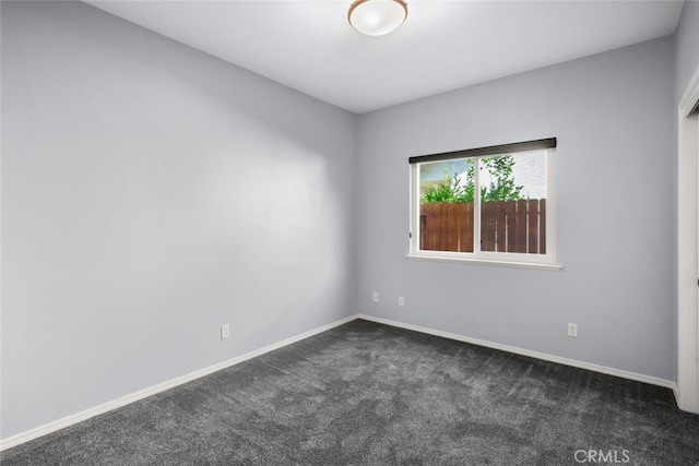 empty room featuring dark colored carpet and baseboards