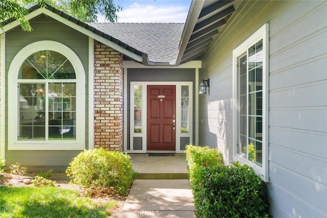 property entrance with roof with shingles and brick siding