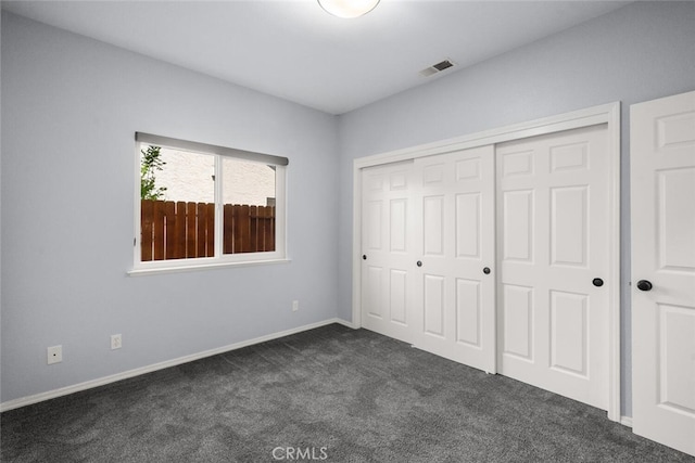 unfurnished bedroom featuring baseboards, dark carpet, a closet, and visible vents