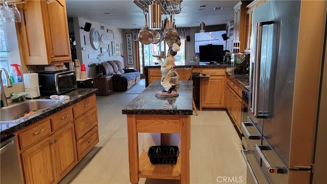 kitchen with stainless steel appliances, open floor plan, a sink, a center island, and dark stone countertops