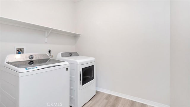 laundry area featuring washing machine and clothes dryer, baseboards, and light wood-style floors