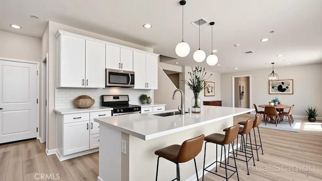 kitchen with appliances with stainless steel finishes, a sink, light wood-type flooring, tasteful backsplash, and light countertops