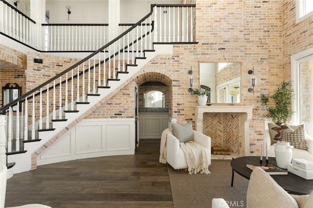 foyer entrance featuring stairs, brick wall, a high ceiling, and dark wood-style floors