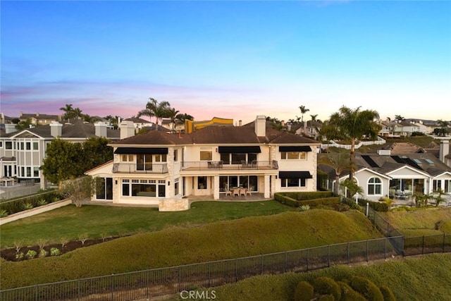 back of property featuring a balcony, a yard, a residential view, a patio, and a fenced backyard
