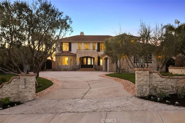 mediterranean / spanish home featuring stone siding, a chimney, and curved driveway