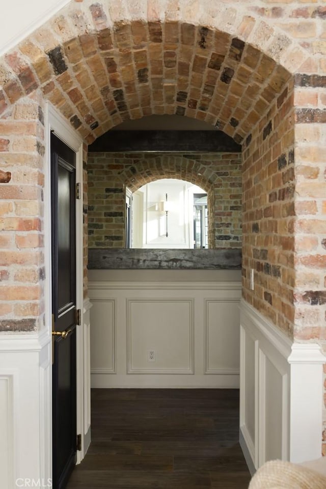 interior space with a wainscoted wall, vaulted ceiling, dark wood-style flooring, and brick wall