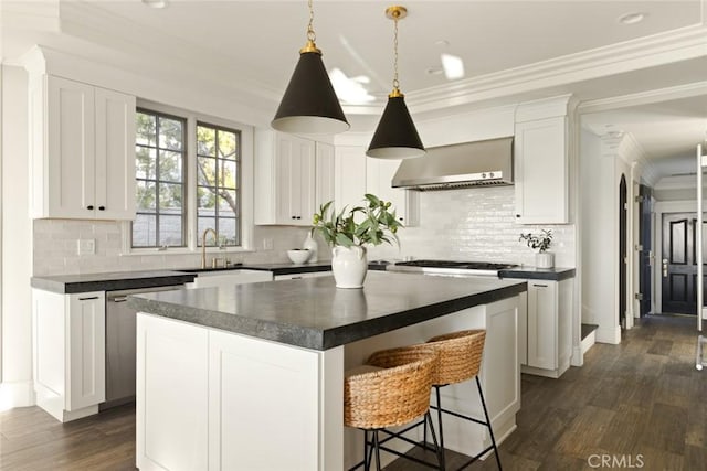 kitchen with a sink, ornamental molding, wall chimney exhaust hood, a center island, and dark countertops