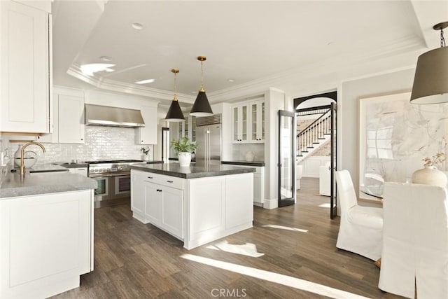 kitchen featuring exhaust hood, built in fridge, a sink, white cabinets, and dark wood-style floors
