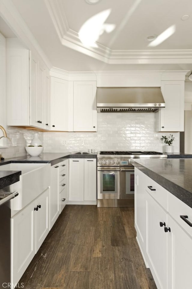 kitchen featuring decorative backsplash, wall chimney exhaust hood, dark countertops, appliances with stainless steel finishes, and dark wood-style floors