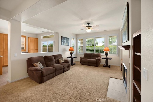 living room featuring a fireplace with flush hearth, light carpet, baseboards, and ceiling fan