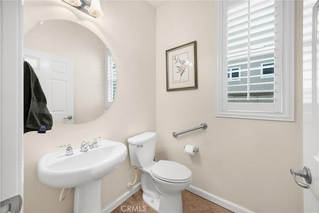 half bath with baseboards, tile patterned flooring, toilet, and a sink