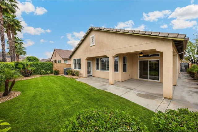 rear view of house featuring a yard, ceiling fan, fence, and stucco siding