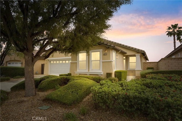 view of property hidden behind natural elements featuring an attached garage, stucco siding, driveway, and fence