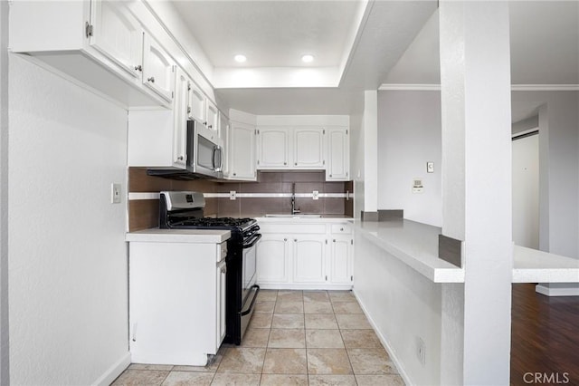 kitchen featuring stainless steel microwave, a sink, tasteful backsplash, white cabinetry, and gas range oven