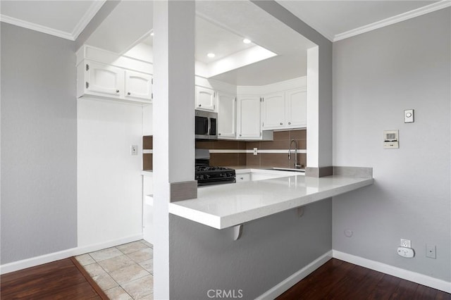 kitchen featuring a peninsula, black gas range oven, a sink, white cabinetry, and stainless steel microwave