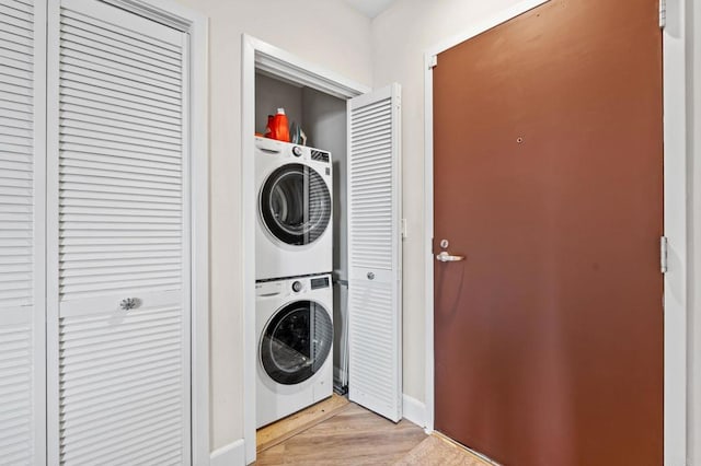 laundry area with laundry area, light wood-style floors, baseboards, and stacked washer and dryer