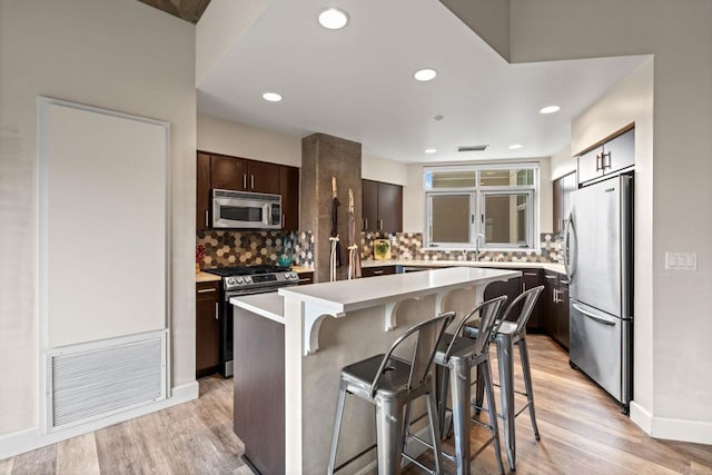 kitchen featuring a breakfast bar area, dark brown cabinets, light wood-type flooring, visible vents, and appliances with stainless steel finishes