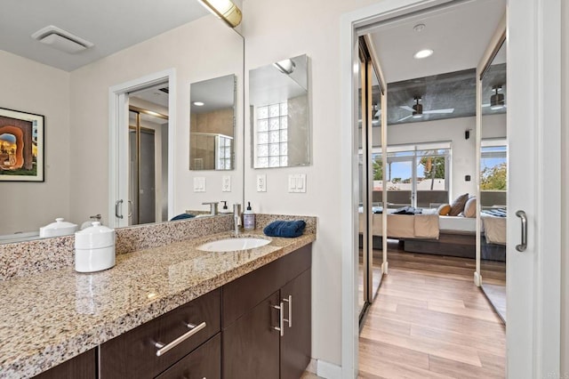 ensuite bathroom with a shower with shower door, wood finished floors, vanity, a ceiling fan, and connected bathroom