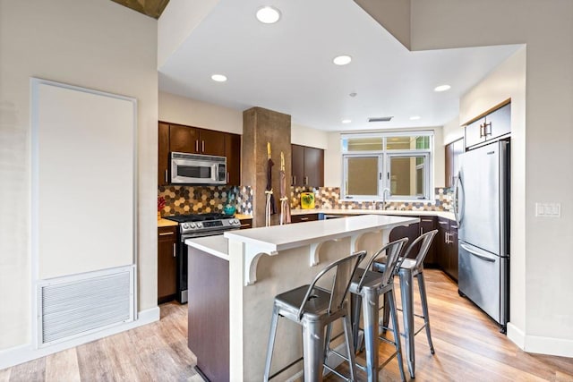3740 Park Blvd Unit 209, San Diego, CA 92103 - kitchen with appliances with stainless steel finishes, a breakfast bar, dark brown cabinetry, light wood finished floors, and decorative backsplash