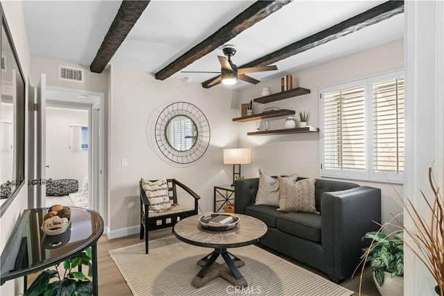 living area featuring wood finished floors, a ceiling fan, visible vents, baseboards, and beamed ceiling