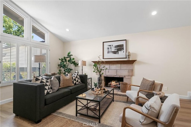 living room featuring wood finished floors, baseboards, vaulted ceiling, a warm lit fireplace, and recessed lighting