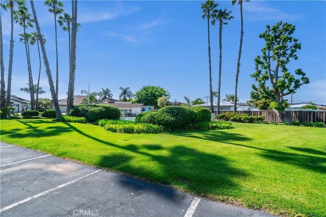 view of home's community with uncovered parking, fence, and a lawn