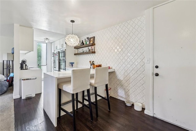 kitchen featuring a kitchen bar, wallpapered walls, white cabinets, dark wood-style flooring, and an accent wall