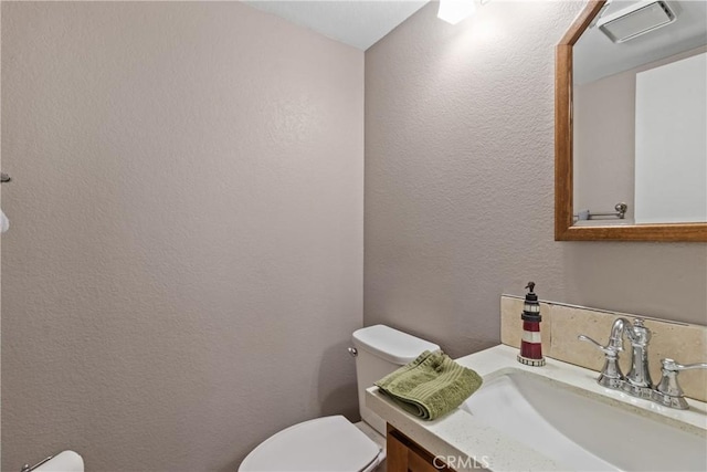 half bathroom with toilet, visible vents, and a textured wall