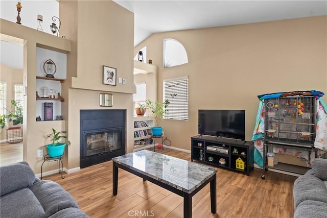 living area featuring baseboards, a glass covered fireplace, and wood finished floors