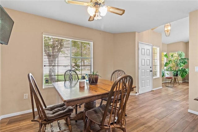 dining space featuring light wood-style floors, baseboards, a ceiling fan, and a healthy amount of sunlight
