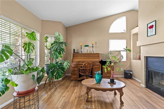 sitting room with baseboards, a glass covered fireplace, plenty of natural light, and wood finished floors