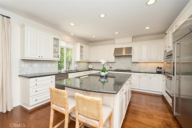 1472 Nicolas Way, Fullerton, CA 92833 - kitchen featuring wall chimney exhaust hood, appliances with stainless steel finishes, dark wood-style flooring, white cabinets, and a breakfast bar