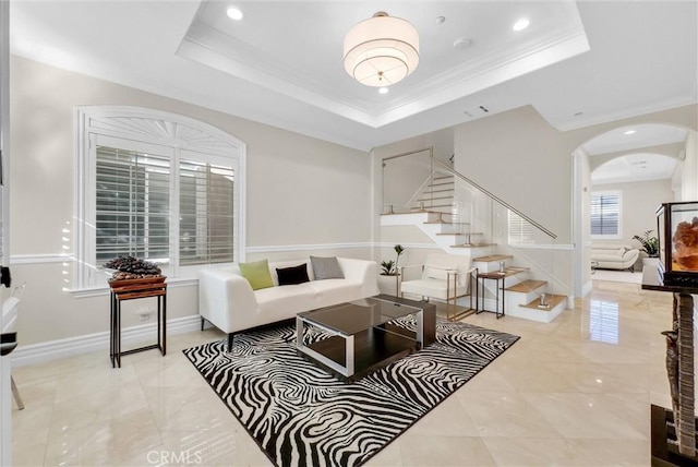 living area with a tray ceiling, recessed lighting, ornamental molding, arched walkways, and stairway