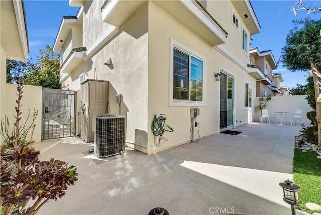 view of home's exterior with a gate, stucco siding, fence, central AC unit, and a patio area